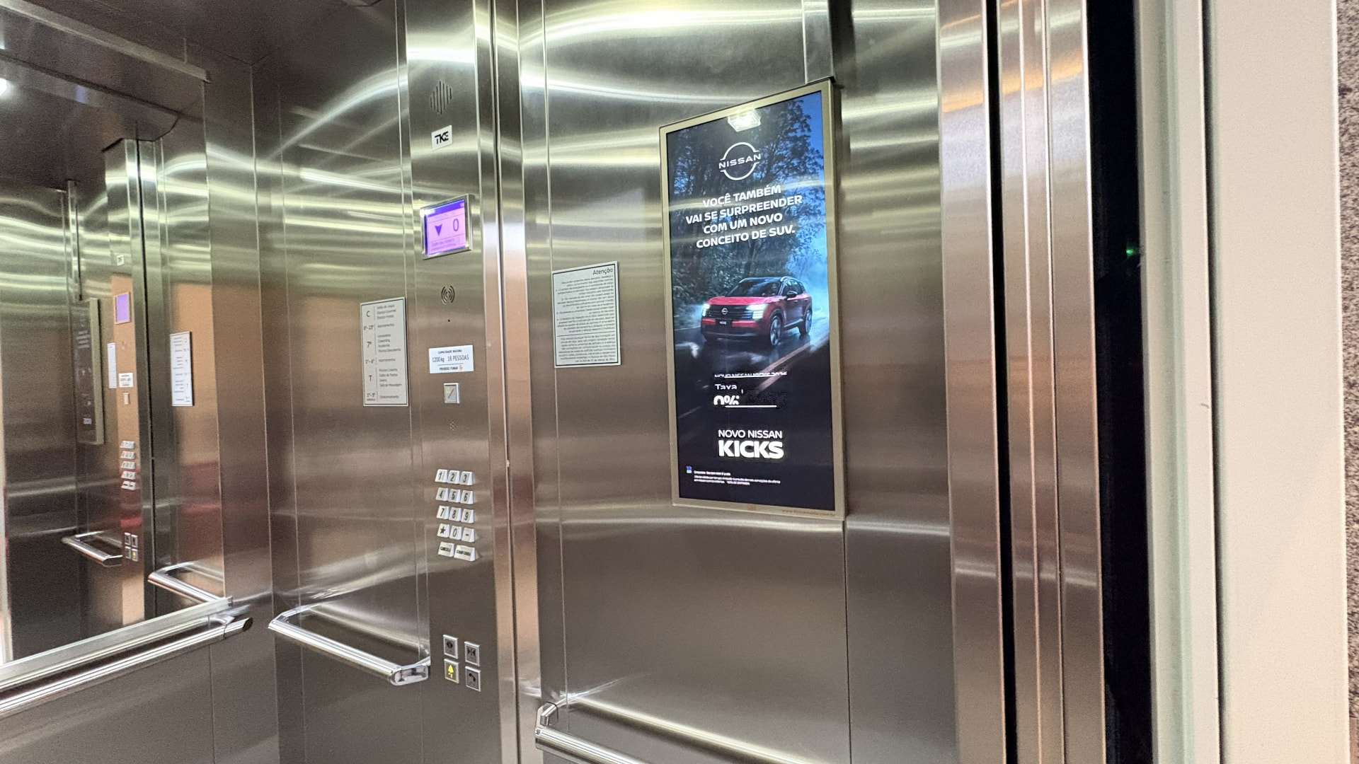 Tela digital Focus Media dentro de elevador exibindo campanha de marca